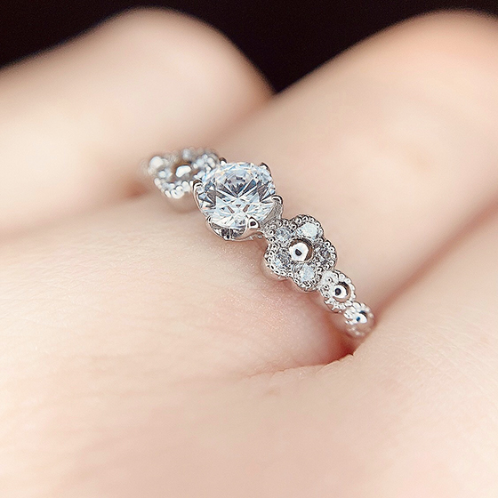 サイドにデザインされたお花のモチーフと縁取りされたミル打ち加工が可愛らしい婚約指輪。