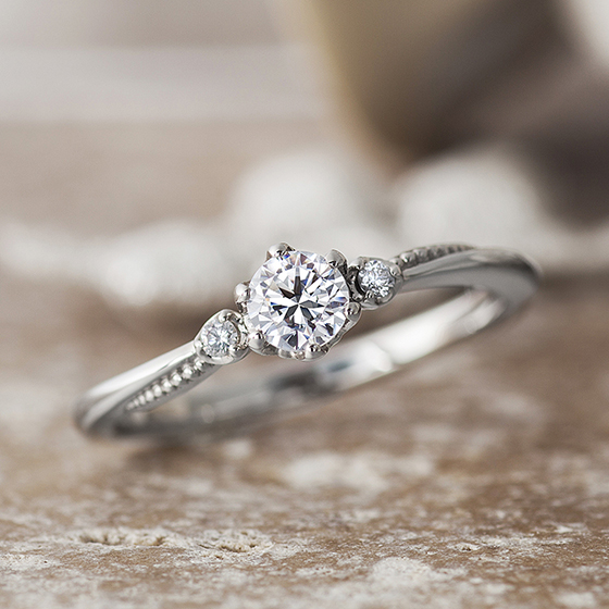 優しいカーブラインを描いた婚約指輪。サイドに施したミル打ちがラインに沿って立体的に見え、丸みのあるデザインを演出しています。
