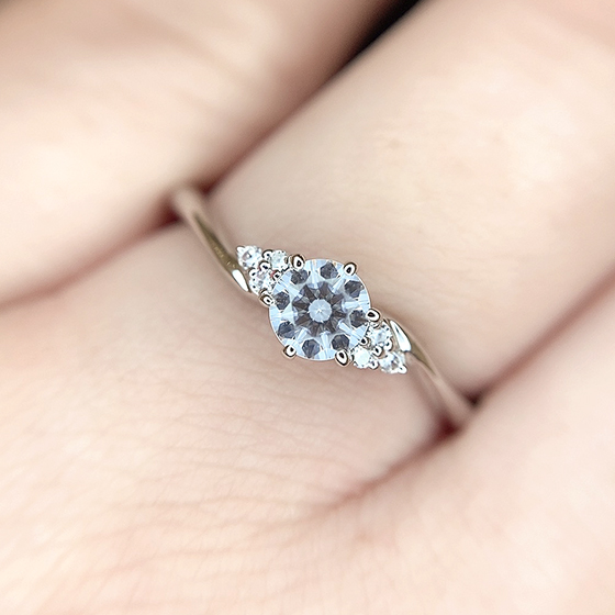 両側に3石ずつ小さなダイヤモンドを施した婚約指輪。カーブラインはシンプルで王道のデザインですがサイドメレに一工夫。