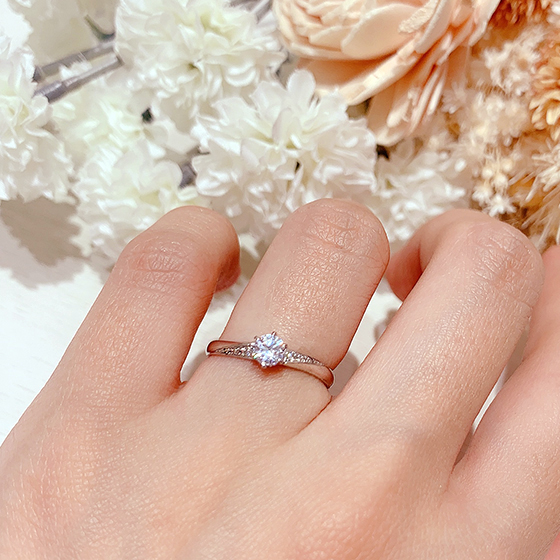 6本爪、ラウンドブリリアントカットのダイヤモンドを留めた人気デザインの婚約指輪です。斜めに流れるようにメレダイヤモンドが上品な印象