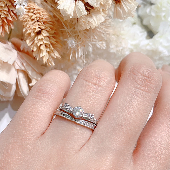 リボンのようなデザインの婚約指輪を重ねることで可愛らしさをプラスしてくれます。