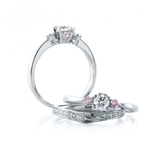 センターダイヤモンドの両サイドにピンクダイヤモンドセッティング。天使の羽をイメージした婚約指輪。メレダイヤモンドが散りばめられた結婚指輪との重ねづけでゴージャスな印象に。